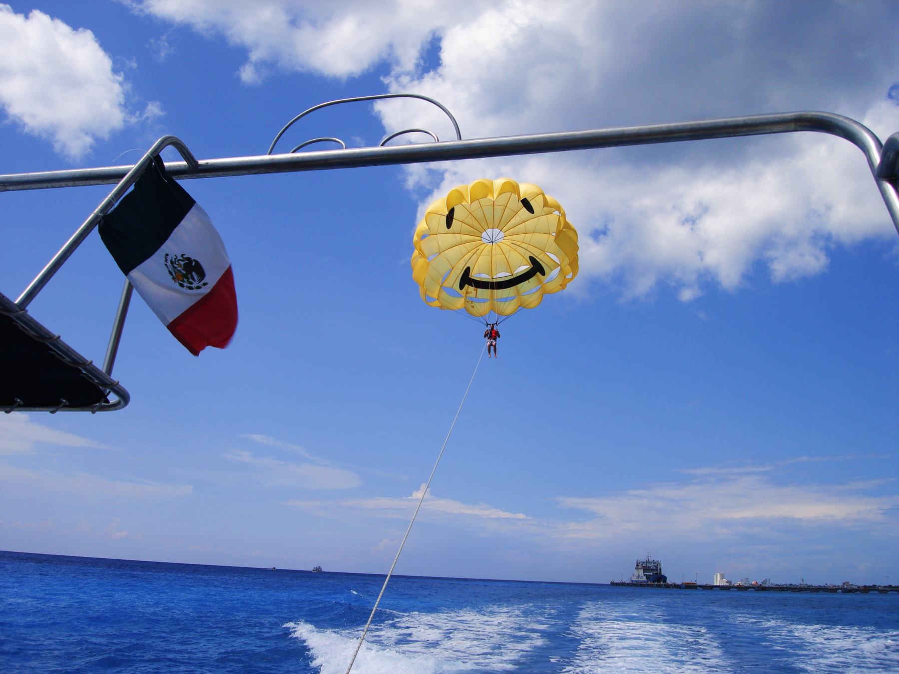 A yellow smiley-face parasail flying above the blue sea off Cozumel, with a Mexican flag on the tow boat
