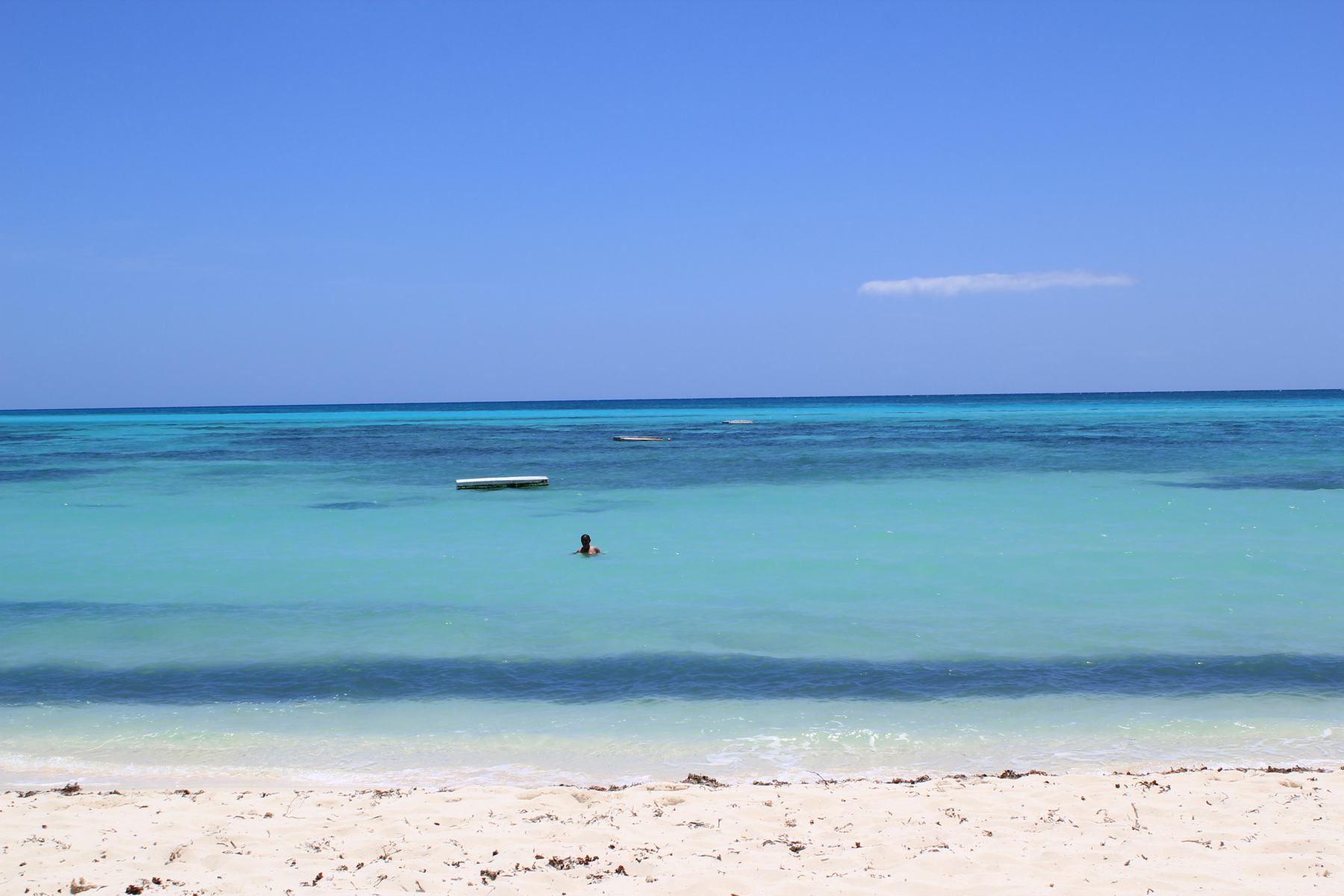 A swimmer in calm, shallow turquoise water off a white-sand beach in Cozumel