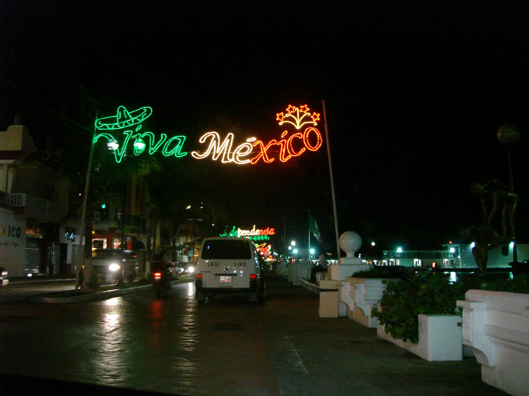 Viva México lights over the waterfront avenue in downtown Cozumel at night, with a taxi on the road